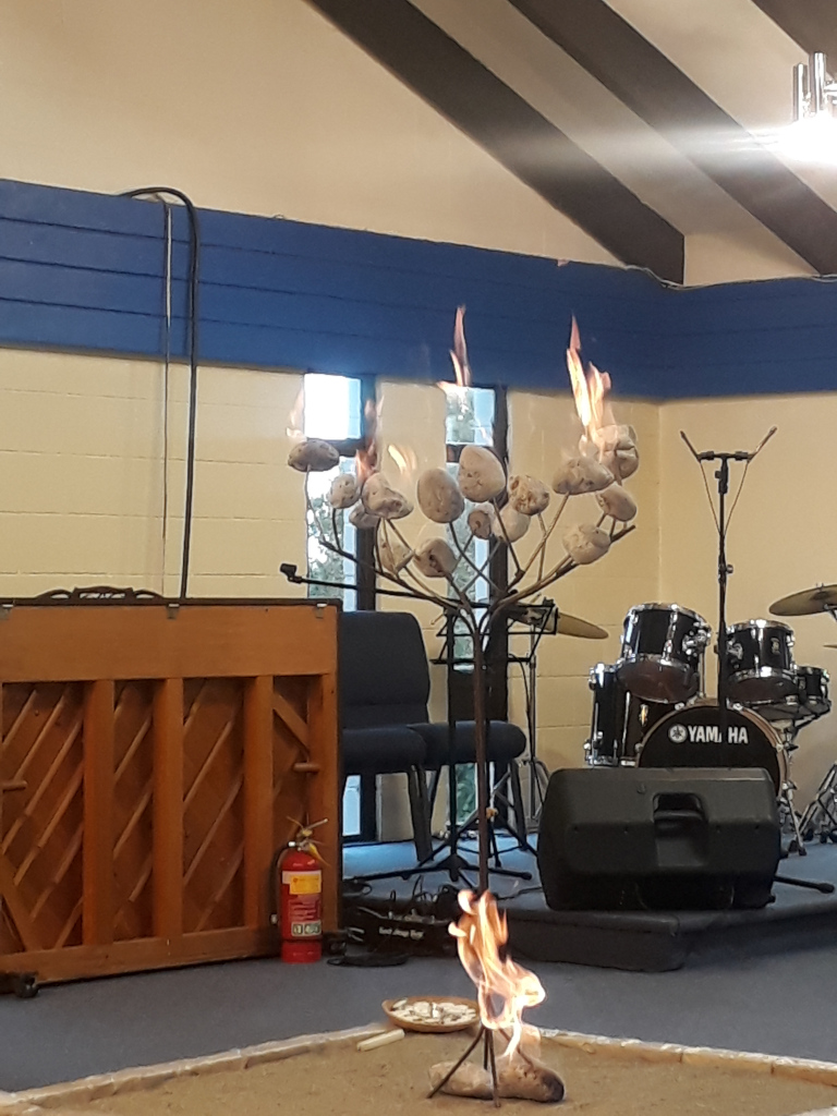 Picture of a metal bush, with pumice, soaked in meths, burning, inside the worship space at St Mary by the Sea